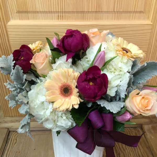 Bouquet of mixed flowers in a white vase with a purple ribbon