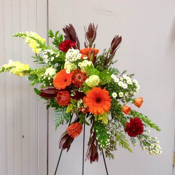 Tall mixed floral arrangement with orange gerberas and red blooms on a stand