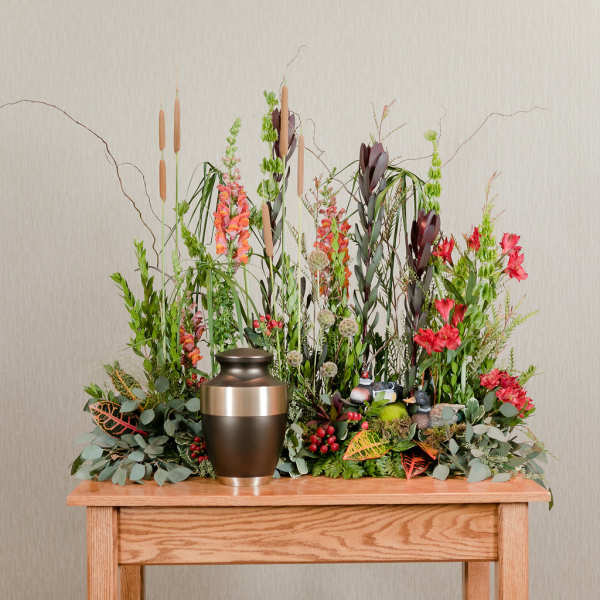 Tall floral arrangement with red and orange blooms in a bronze urn