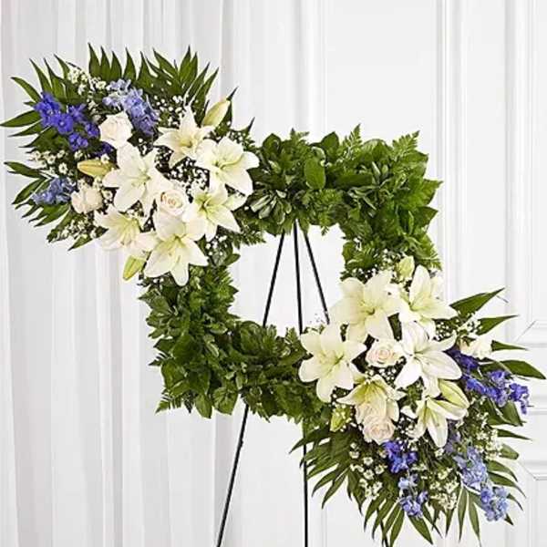 Two floral wreaths on black stands with white lilies and blue flowers