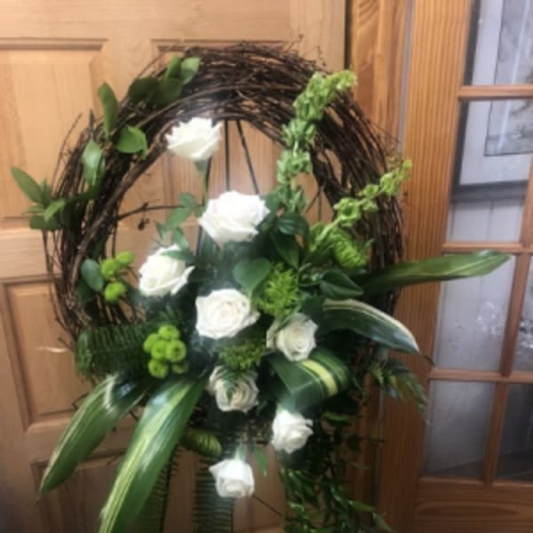 Standing grapevine wreath with white roses and green floral accents on a metal easel