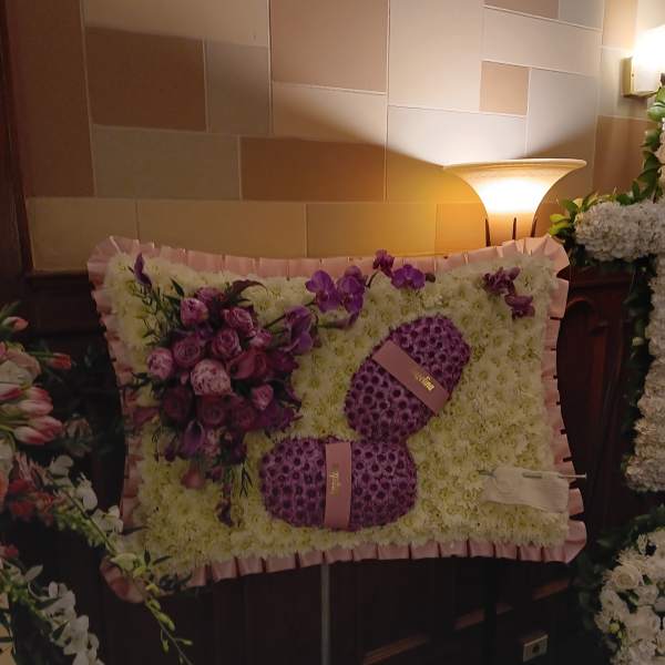 Large floral tribute with purple flowers and white blooms on a pink-framed panel