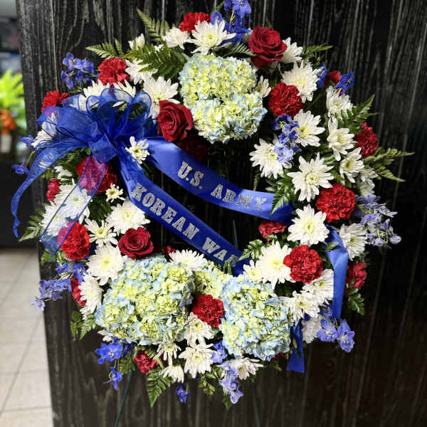 Patriotic funeral wreath with red, white, and blue flowers and a blue ribbon