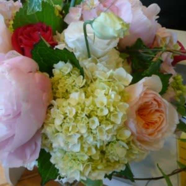 Round arrangement of pale pink peonies, roses, and cream hydrangeas with accents of red roses