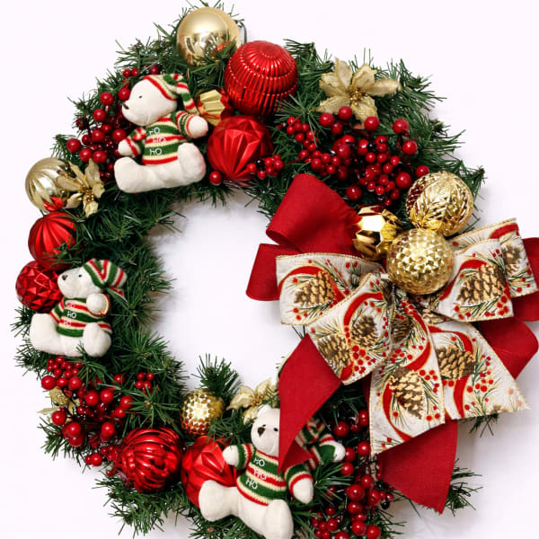 Decorative Christmas wreath with plush bears, red berries, red and gold ornaments, and a large red ribbon bow.