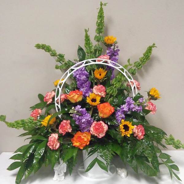 Colorful floral arrangement with sunflowers, roses, carnations, and purple blooms in a white basket
