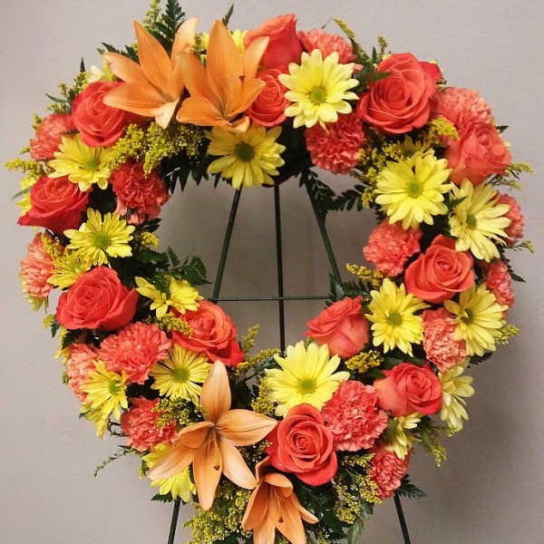 Heart-shaped floral wreath with roses, daisies, carnations, and lilies on a stand