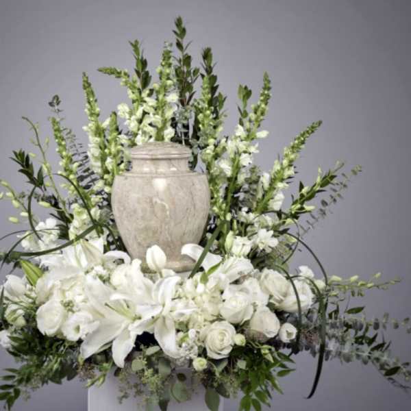 White floral arrangement with lilies and roses around a stone urn