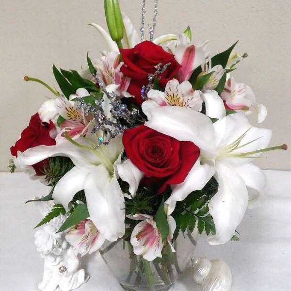 Red roses and white lilies in a clear glass vase with silver accents