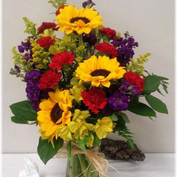 Bouquet of sunflowers, red carnations, and purple flowers in a glass vase