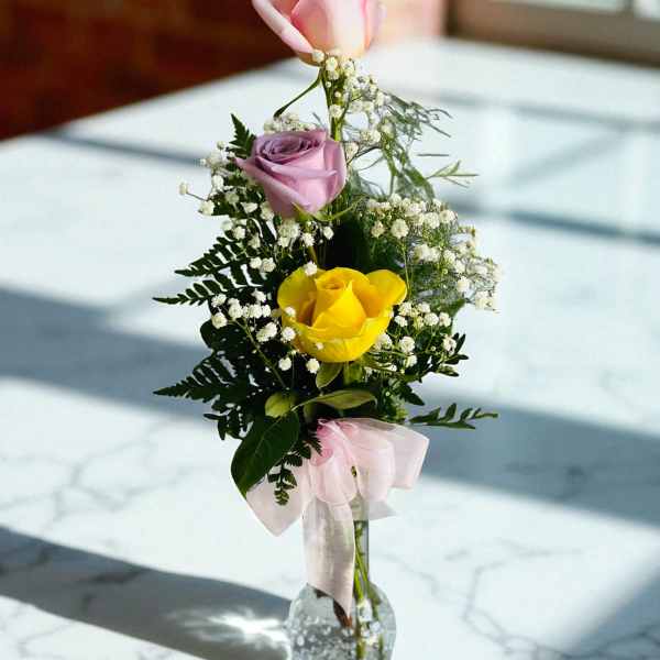 Pink, lavender, and yellow roses in a clear glass vase with a pink ribbon