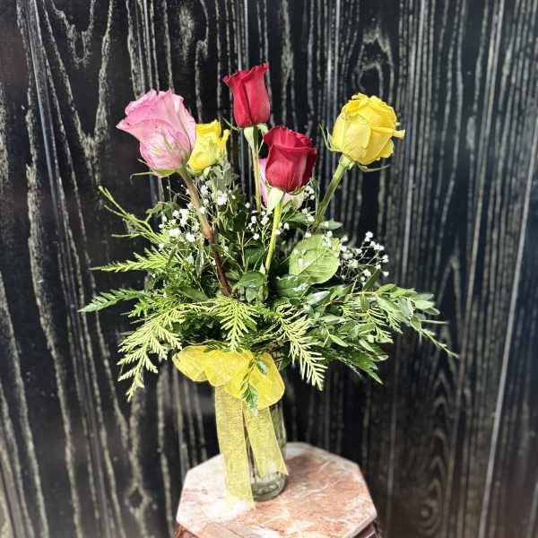 Bouquet of pink, red, and yellow roses in a glass vase with a yellow ribbon