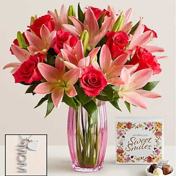 Pink lilies and red roses in a tall glass vase with a card and chocolates