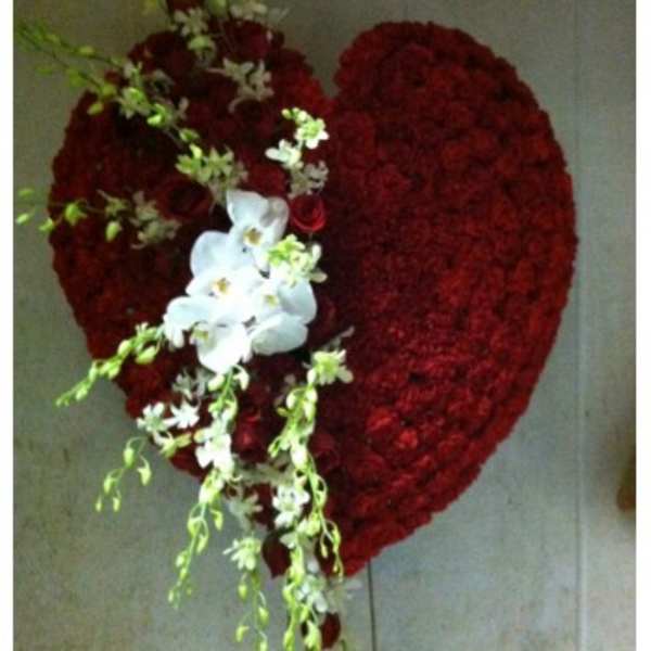 Heart-shaped red floral arrangement with white orchids and trailing greenery