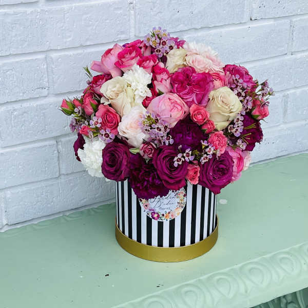 Round bouquet of pink, white, and magenta roses in a striped hatbox