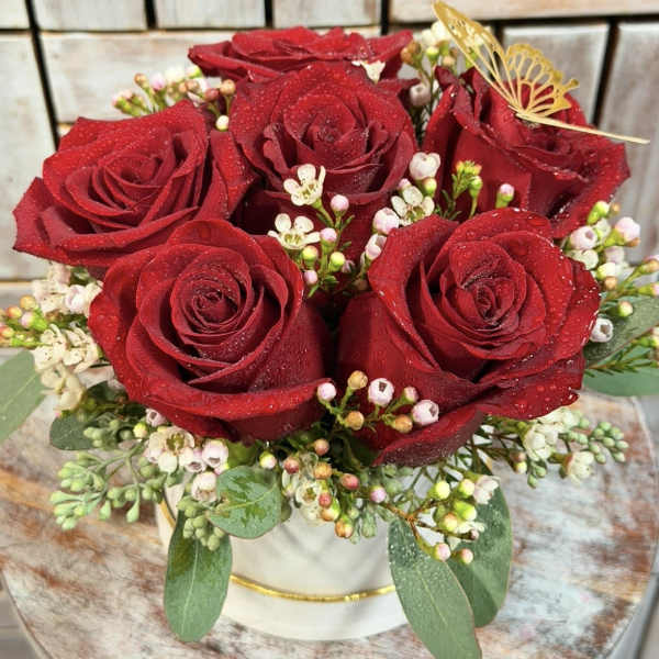Red roses arranged in a white hat box with small white filler flowers