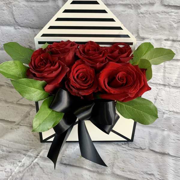 Red roses arranged in a striped gift box with a black ribbon