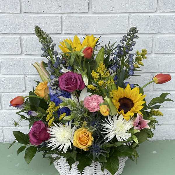 Mixed bouquet in a white basket with sunflowers, roses, and lilies