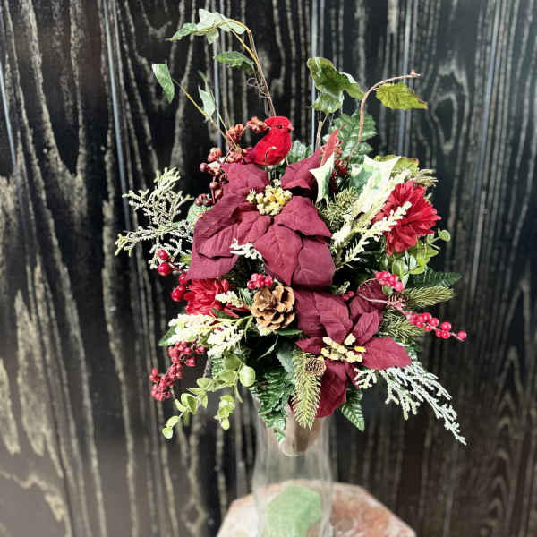 Holiday floral arrangement in a clear glass vase with red blooms and berries