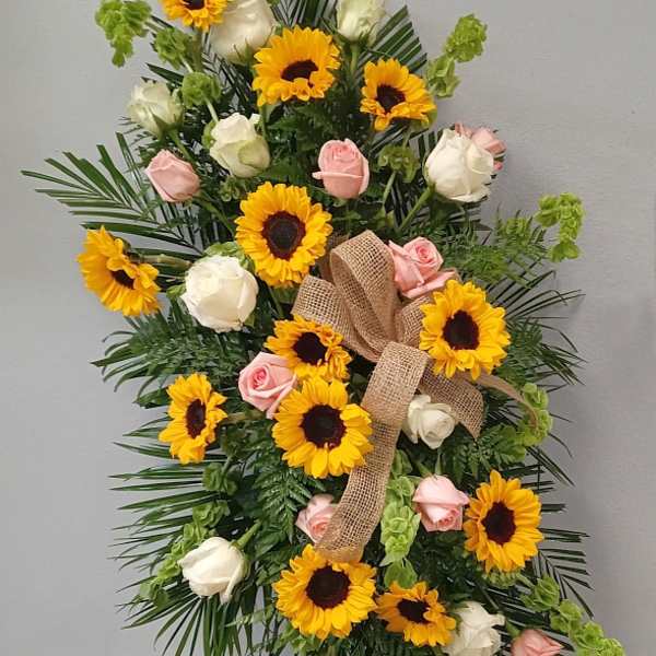Standing floral spray with sunflowers, pink and white roses, and a burlap bow