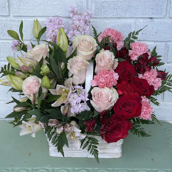 Mixed bouquet of pink and red roses, lilies, and carnations in a white basket