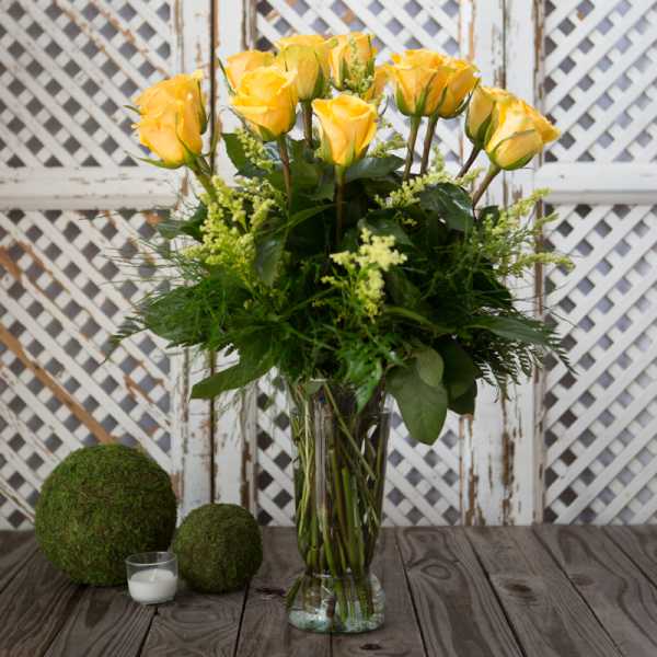 Yellow roses in a clear glass vase with greenery.