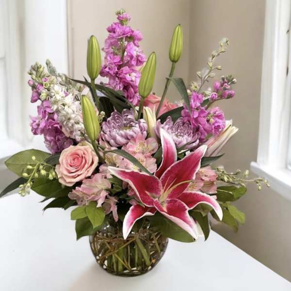 Pink lilies and roses in a glass vase with purple flowers