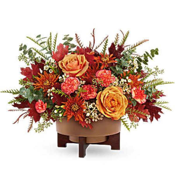 Autumn floral arrangement with orange roses and red blooms in a low container