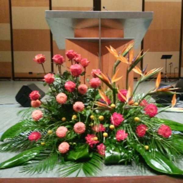 Large stage arrangement with pink roses, round pink blooms and orange tropical flowers in front of a podium