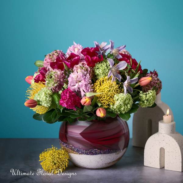 Mixed bouquet in a round glass vase beside a lit candle