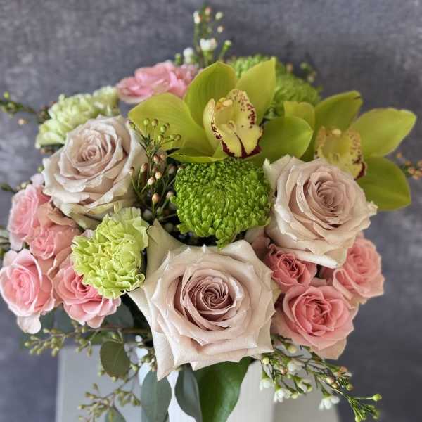 Arrangement of blush and pink roses, green orchids, and green mums in a white vase