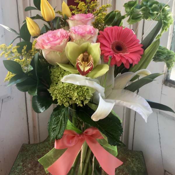 Mixed bouquet in a glass vase with pink roses, yellow tulips, and a pink gerbera daisy