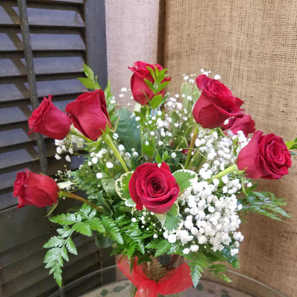 Medium bouquet of red roses with white filler flowers in a clear glass vase tied with a red ribbon.