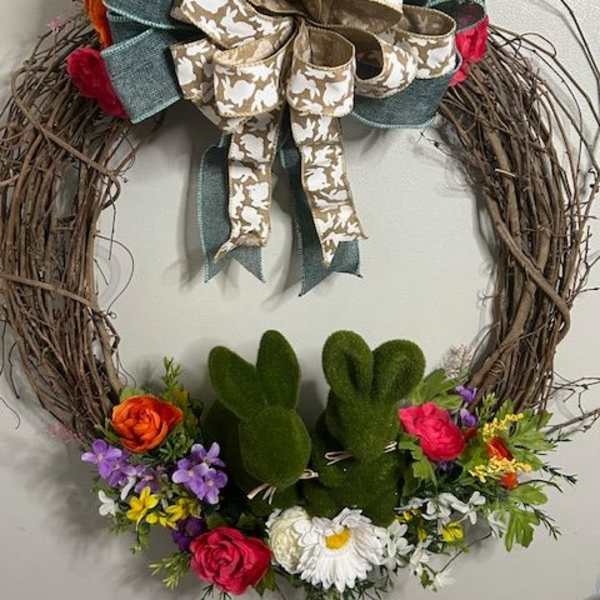 Floral grapevine wreath with a large ribbon bow and two green bunny figures
