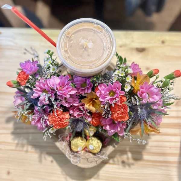 Flower arrangement around a drink cup with a red straw and chocolates below