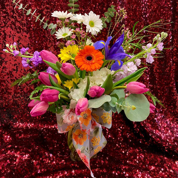 Bright mixed bouquet with pink tulips, daisies, iris and gerbera in a glass vase with a floral bow.