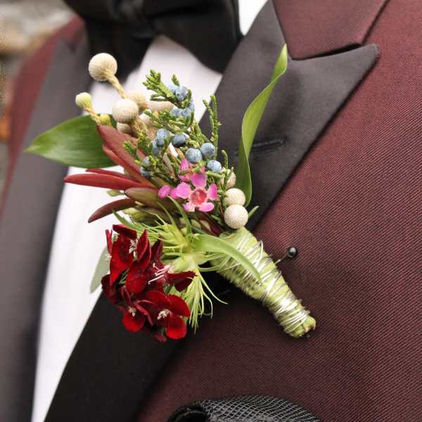 Boutonniere with red flowers and blue berries on a suit lapel