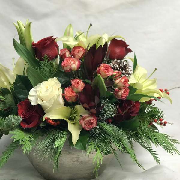 Holiday floral arrangement with roses, lilies, and greenery in a round vase