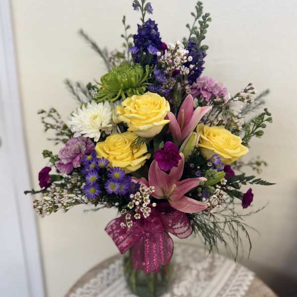 Mixed bouquet of yellow roses, pink lilies, and purple flowers in a glass vase