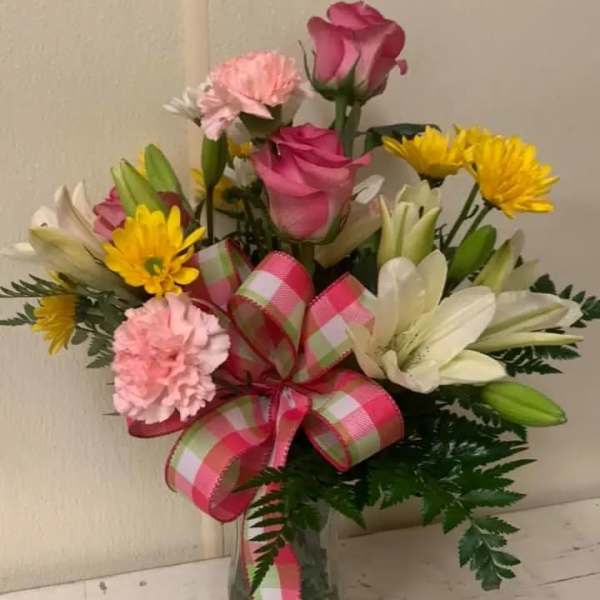 Bouquet of pink roses, lilies, and yellow daisies in a glass vase with a plaid ribbon