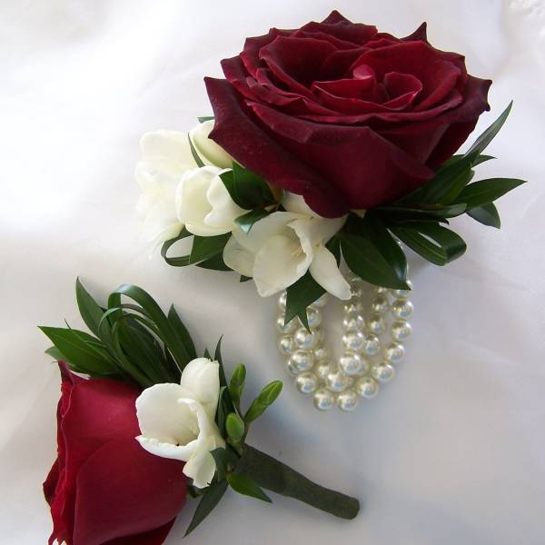 Two red rose boutonnieres with white accents and pearl strands