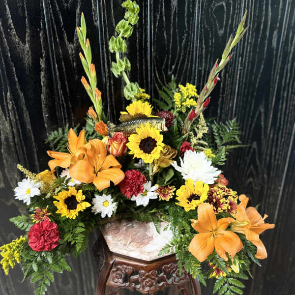 Orange lilies and mixed flowers arranged around a fish centerpiece in a vase