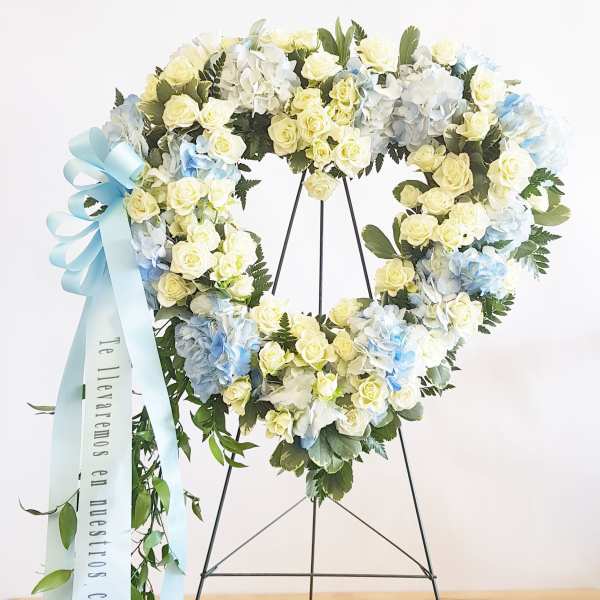 Heart-shaped floral wreath with pale roses, hydrangeas, and a blue ribbon