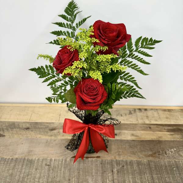 Three red roses with yellow filler in a black wrap and red bow