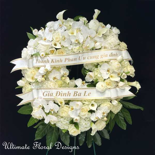 White funeral wreath with orchids, roses, and calla lilies on a black background