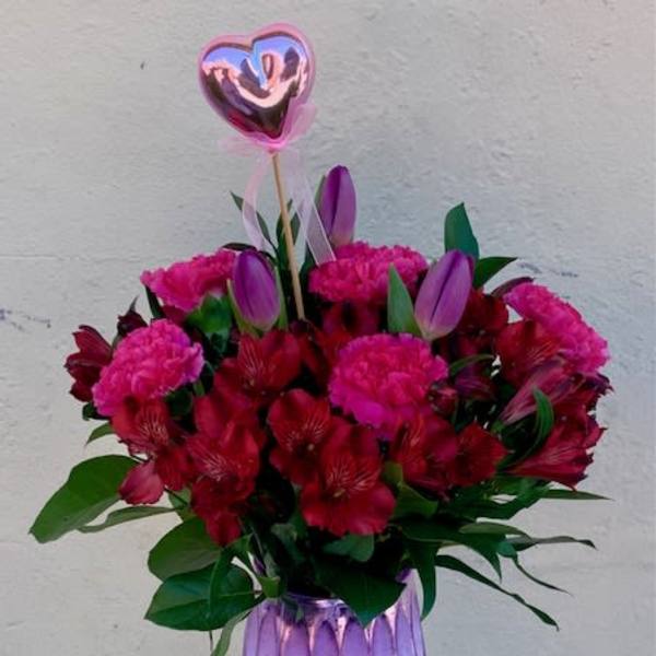 Bouquet of red and pink flowers in a purple vase with a heart balloon