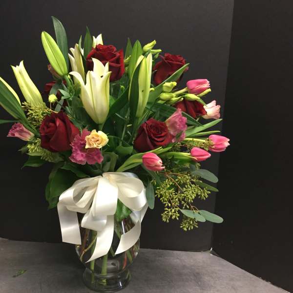 Bouquet of red roses, white lilies, and pink tulips in a glass vase with a white ribbon