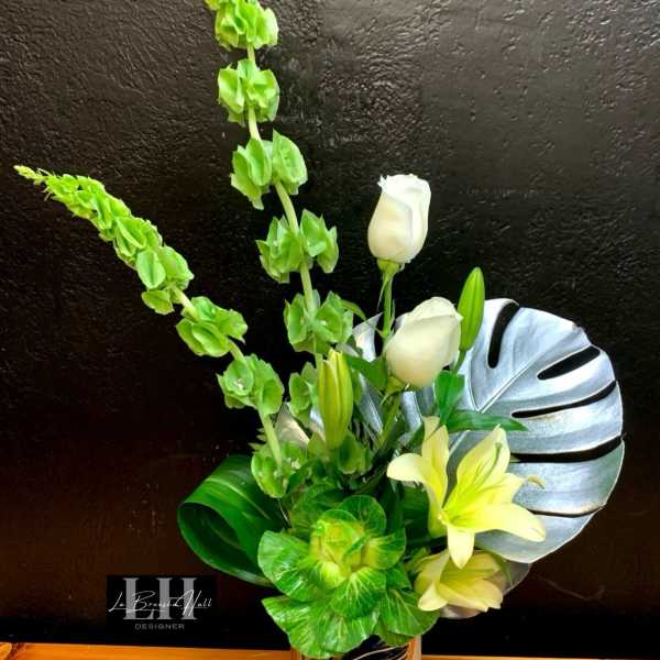 White lilies and green flowers in a silver vase with a large leaf accent