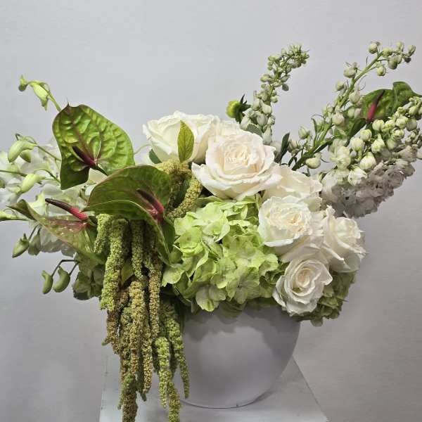 White roses and green hydrangeas in a white vase with trailing greenery