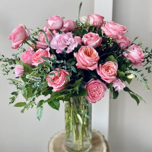 Pink roses arranged in a clear glass vase with greenery